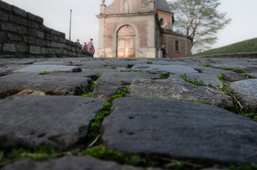 Fototapeta na wymiar Cobblestone road with grass and moss leading to a chapel