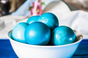 Painted, blue, Easter eggs. Festive blue and wooden table. White deep plate with a symbol of Easter. The combination of blue shades.
