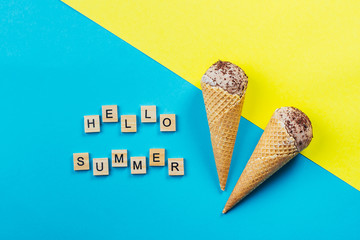 Chocolate Ice cream in waffle cone on blue and yellow background. Dessert, summer card concept. Wooden letters words Hello Summer. Top view, flat lay.