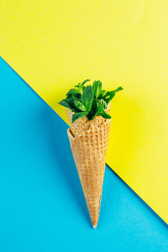 Ice cream waffle cone with mint leaves on blue yellow background. Summer card concept. Minimal Creative idea. Top view, flat lay, copy space