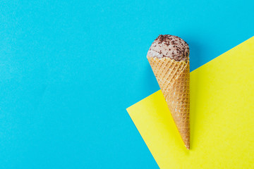 Summer Food Background. Chocolate ice cream in waffle cone on blue yellow background. Copy space, top view