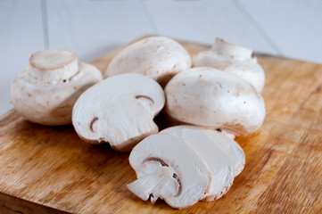 Fresh champignons on a wooden cutting board.On white wooden background.