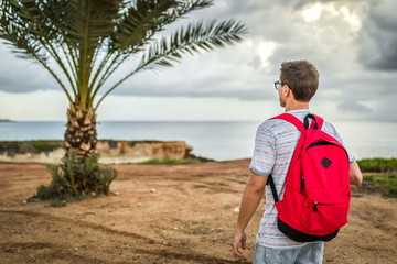 Traveler guy with red backpack lifestyle walking, summer outdoor palm