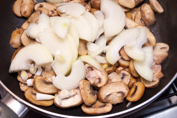 Fresh champignons and onions are fried in a pan. Top view.
