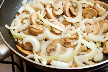 Fresh champignons and onions are fried in a pan. Home kitchen.