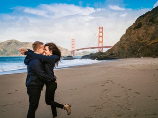 Loving couple man and woman hugging on beach in San Francisco on Golden gate bridge background on...