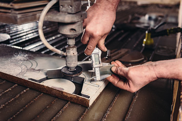 Worker at water jet cutter checking measures with digital caliper