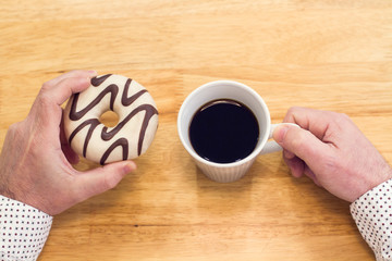 Manos de hombre comiendo un donuts con taza de café sobre una mesa de madera. Vista superior y de cerca. Copy space