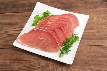 Uncooked defrosted pork slices with greens on the square dish