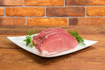 Uncooked defrosted pork slices with greens on the square dish