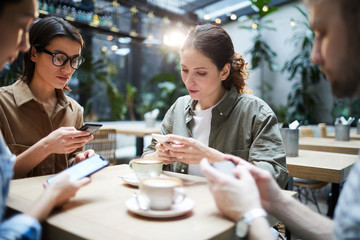 Group of serious gadget-addicted startuppers sitting at table and using smartphones while searching for information to solve problem