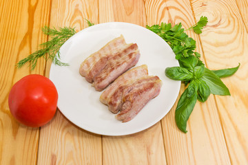 Grilled streaky bacon on white dish, fresh tomato and greens