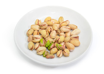 Partly peeled roasted salted pistachio nuts on the white saucer