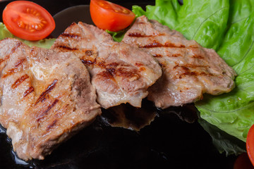 Grilled sappy pork steaks with vegetables on black dish closeup