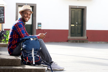 Full body happy african american travel man relaxing with cellphone and bag on street