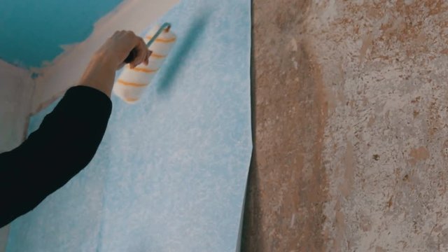 Woman hand sheet of blue papper wallpaper is glued to the wall with a special construction roller
