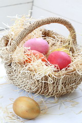 Basket with painted eggs on a white wooden background
