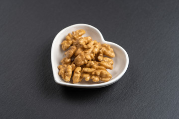 A few shelled walnuts lie in a saucer in the shape of a heart on textured slate board