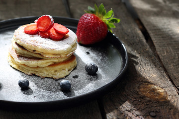 Pancakes with strawberries, blueberries and powdered sugar. Sweet breakfast.