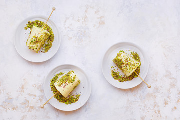 Cardamom and pistachio nut kulfi, Indian  ice cream served on white plates, textured surface. Top view, blank space - obrazy, fototapety, plakaty