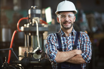 Waist up portrait of mature factory worker wearing hardhat looking at camera while standing in...