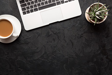 Top view of office desk. Green plant in a pot, cup of coffee and modern silver laptop on dark background. Copy space for your text