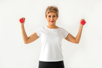 stylish elderly woman in age stands playing sports with dumbbells on a white background