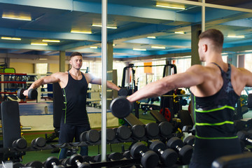 Fototapeta na wymiar muscular man training in the gym. young guy picks up a dumbbell near the mirror.