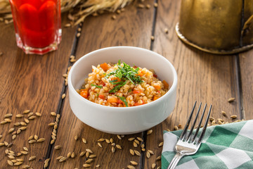 Bulgur with tomatoes and squash and glass of berry drink on wooden table