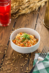 Bulgur with tomatoes and squash and glass of berry drink on wooden table