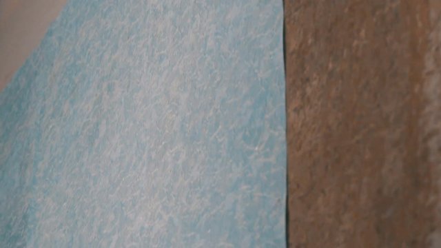 Close up of sheet of blue papper wallpaper is glued to the wall with a special construction roller