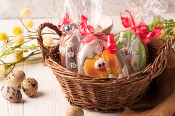 wicker brown basket with wrapped easter cookies near quail eggs and blossoming branch on wooden surface
