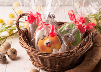 wicker basket with wrapped easter cookies near quail eggs and blossoming branch on wooden surface