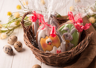 easter brown wrapped cookies in a brown wicker basket near quail eggs and blossoming branch on wooden white surface