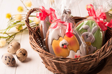 Fototapeta na wymiar easter green and yellow wrapped cookies in a brown wicker basket near quail eggs and blossoming branch on wooden white surface