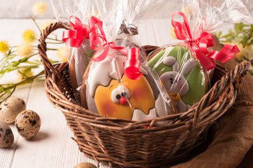 easter wrapped cookies in a brown wicker basket near quail eggs and blossoming branch on wooden white surface