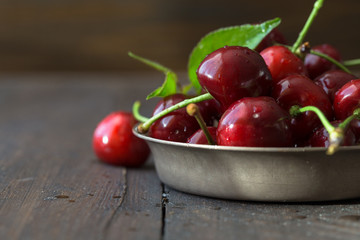 White cup with ripe berries of yellow and red sweet cherries and several fruit with green leaf of cherry tree on wooden background
