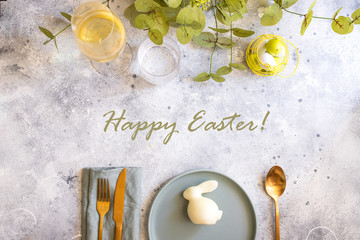 Beautiful Easter table setting in Scandinavian style. Green mint plate with bunny, painted  egg and  cold cutlery on modern concrete background decorated with plant. Copy space.Top view