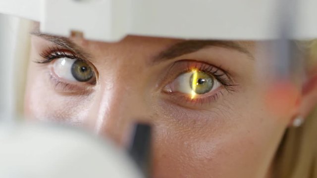 PAN with extreme close up of doctor off camera using slit lamp microscope to check eyesight of woman