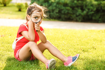 Positive cheerful little girl looking through a magnifying glass outdoors