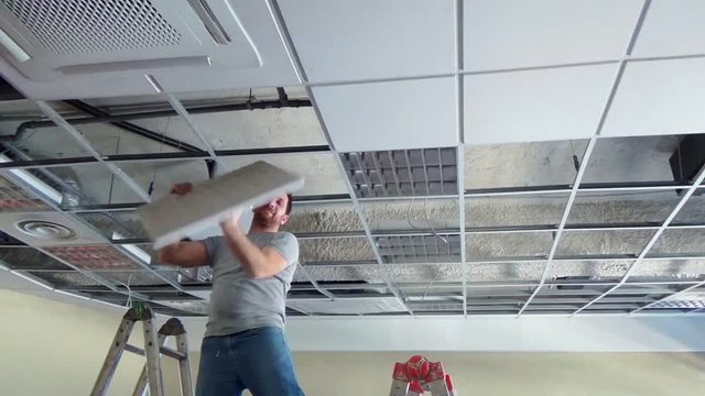 Construction worker performs a suspended ceiling maintenance with mineral fiber squares.