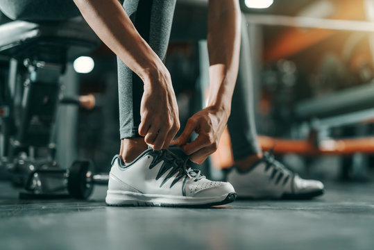 Close up of slim Caucasian woman tying shoelace in gym at night. Be stronger than your excuses.