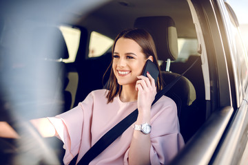 Portrait of gorgeous brunette with big toothy smile driving car and using smart phone.