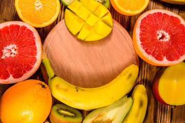 Still life with exotic fruits and cutting board. Bananas, mango, oranges, avocado, grapefruit and kiwi fruits on wooden table. Top view