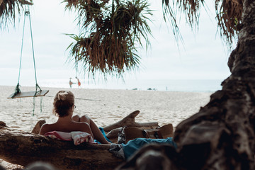 Back view of woman lying on the log and watching something in front of her on tropical beach.