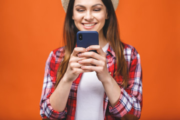 Photo of cheerful cute beautiful young woman chatting by mobile phone isolated over orange wall background.