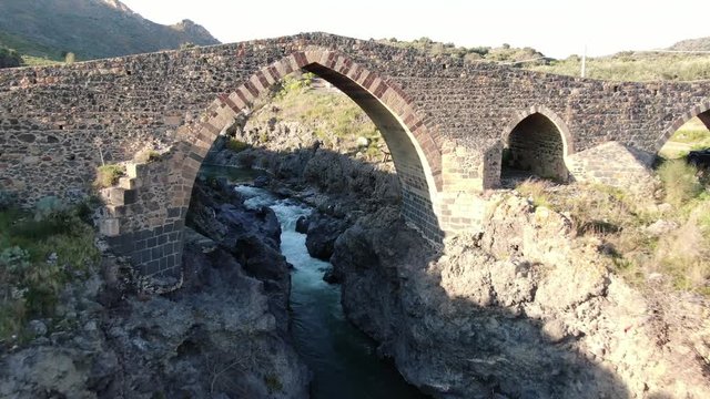 drone flyng up the river thru an ancient bridge in sicily