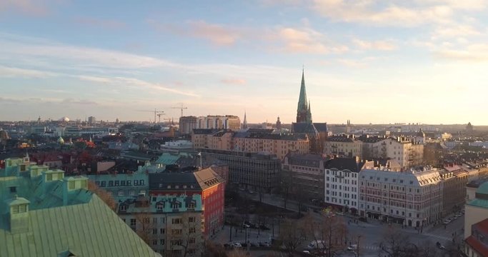 Beautiful aerial view early spring sunset Stockholm Sweden. Drone flies backward low over old Swedish roofs. Colorful urban skyline horizon. Stunning golden hour cityscape.