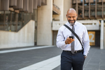 Satisfied businessman walking while using phone
