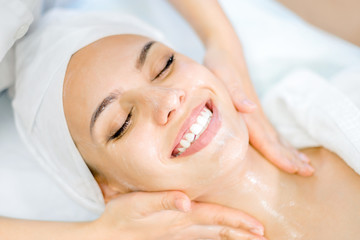 Cosmetology. The hands of a cosmetologist do a facial massage with a mask. Smiling girl on spa...